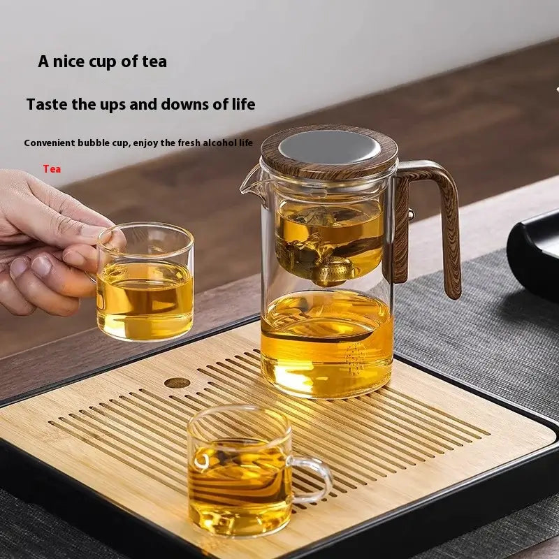 Hand pouring tea from a glass teapot into a cup, showcasing a delicate brewing setup.