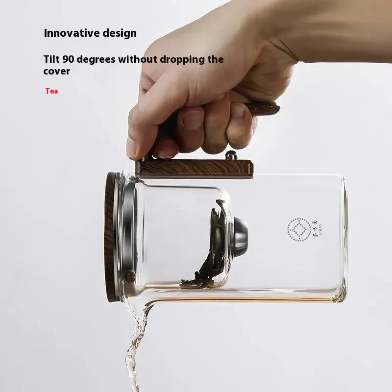 Person holding an elegant glass teapot with a wooden handle, demonstrating innovative design for easy pouring.